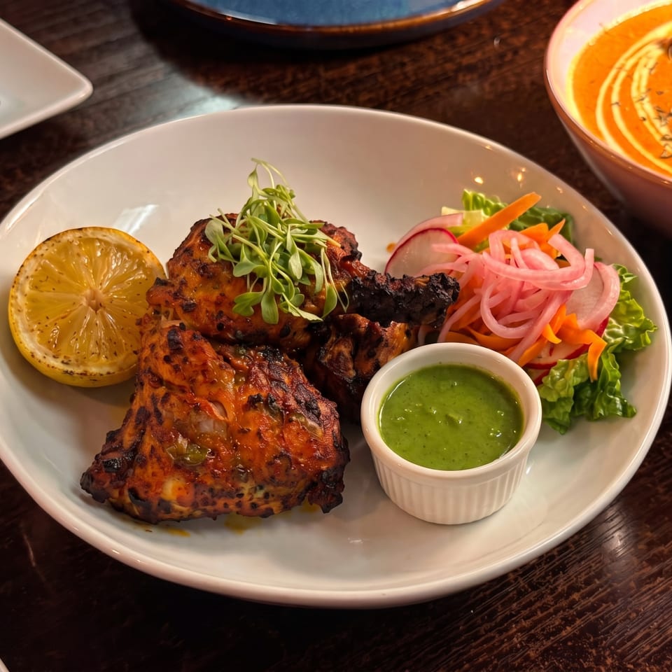 Tandoori chicken with lemon, green chutney, and pickled salad on a white plate.